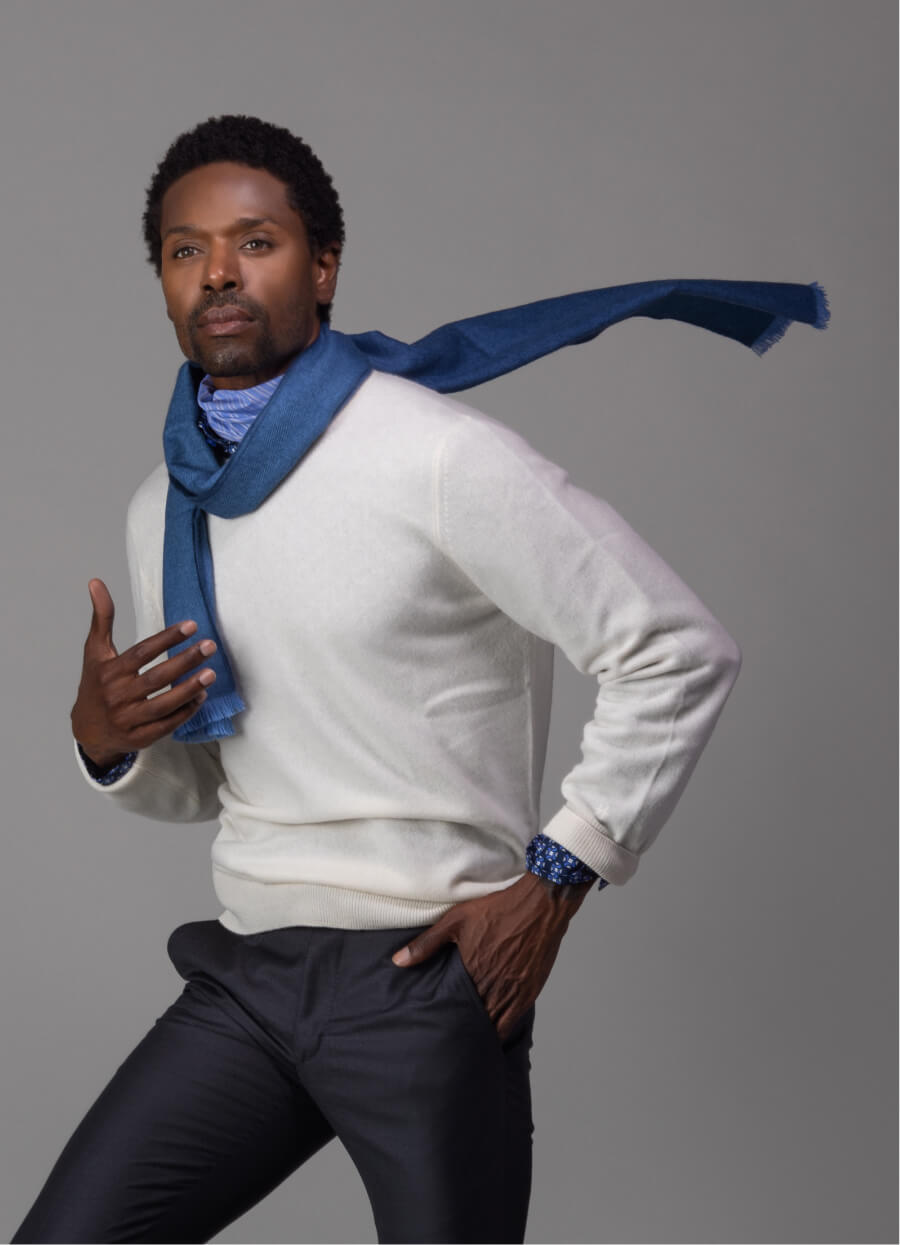 Model wearing white Ike Behar sweater and blue scarf against gray background