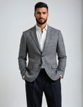 Man wearing a gray blazer over a white shirt with black pants on a light gray background