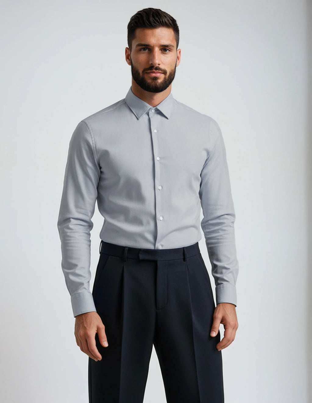 Man wearing a light gray dress shirt and dark pants against a plain background