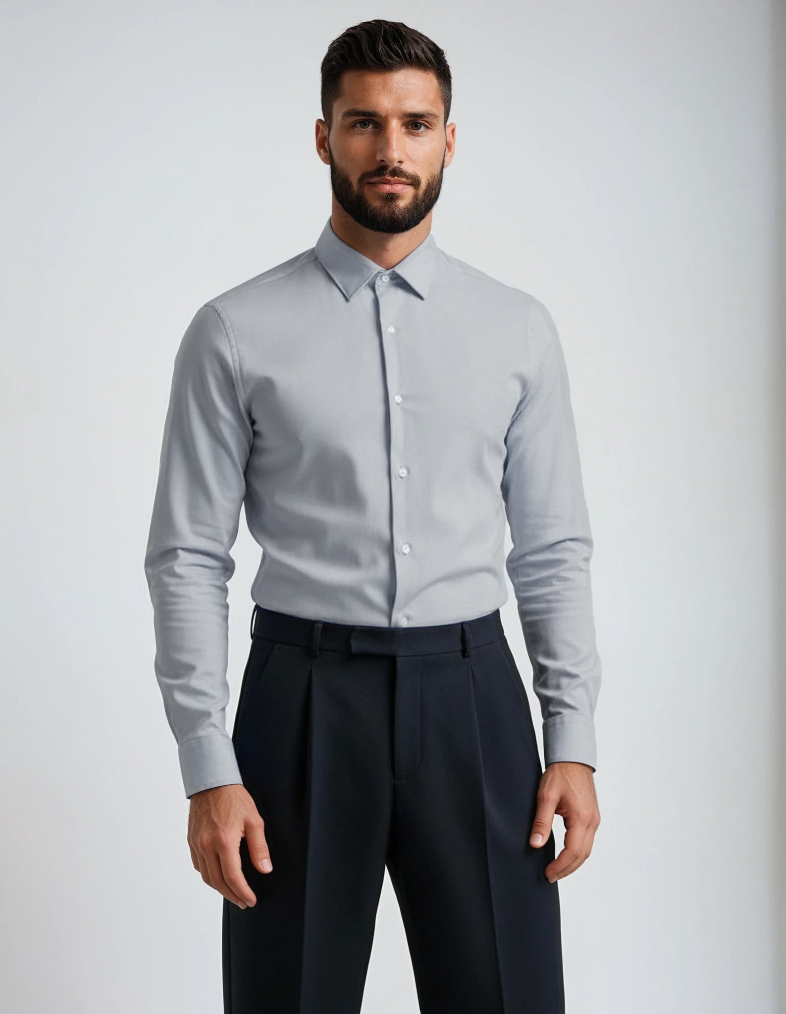 Man wearing a light gray dress shirt and dark pants against a plain background