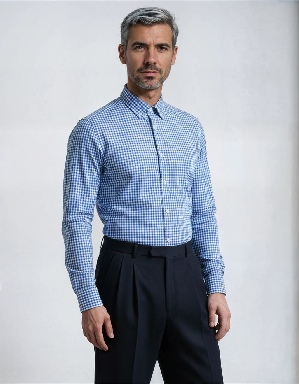 Man wearing a blue checkered shirt and dark pants against a light gray background