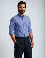 Man wearing a blue checkered shirt and dark pants against a light gray background