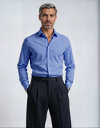 Man wearing a blue dress shirt and black pants against a light gray background