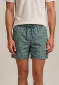 Man wearing a light-colored polo shirt and green patterned shorts on a plain background