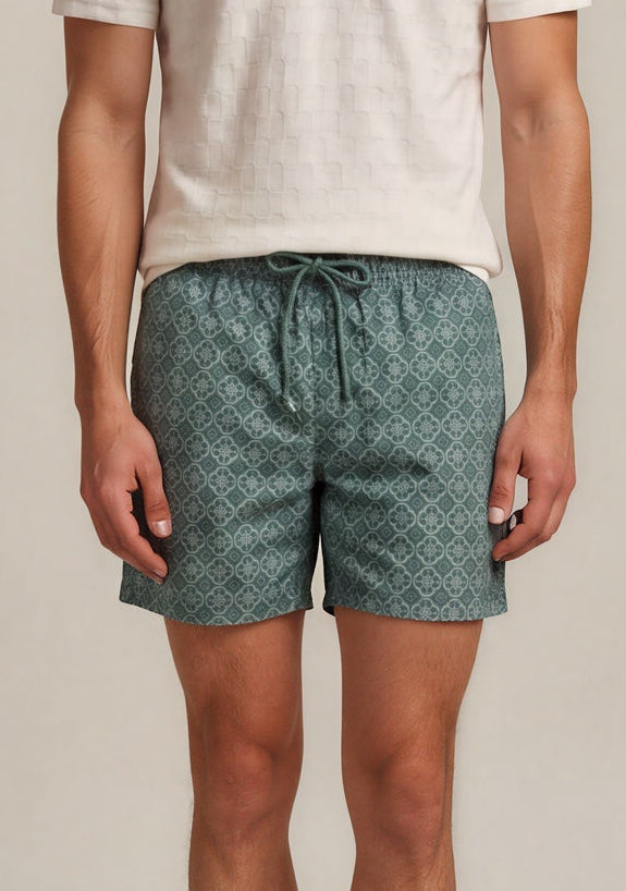 Man wearing a light-colored polo shirt and green patterned shorts on a plain background