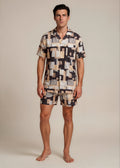 Man wearing a patterned shirt and shorts set against a plain background