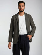 Man wearing a gray and brown blazer over a white shirt and dark pants on a light gray background