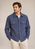 Man in denim knit shirt jacket and khaki pants in front of tan background.