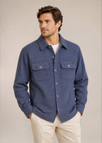 Man in denim knit shirt jacket and khaki pants in front of tan background.