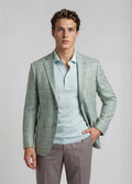 Man wearing a light green checkered blazer over a light blue shirt with gray pants on a plain background