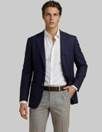 Man wearing a navy blazer, white shirt, and light gray pants on a beige background