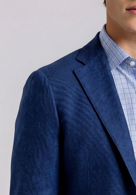 Man wearing a blue blazer over a light blue shirt and white pants on a plain background
