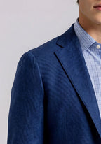 Man wearing a blue blazer over a light blue shirt and white pants on a plain background