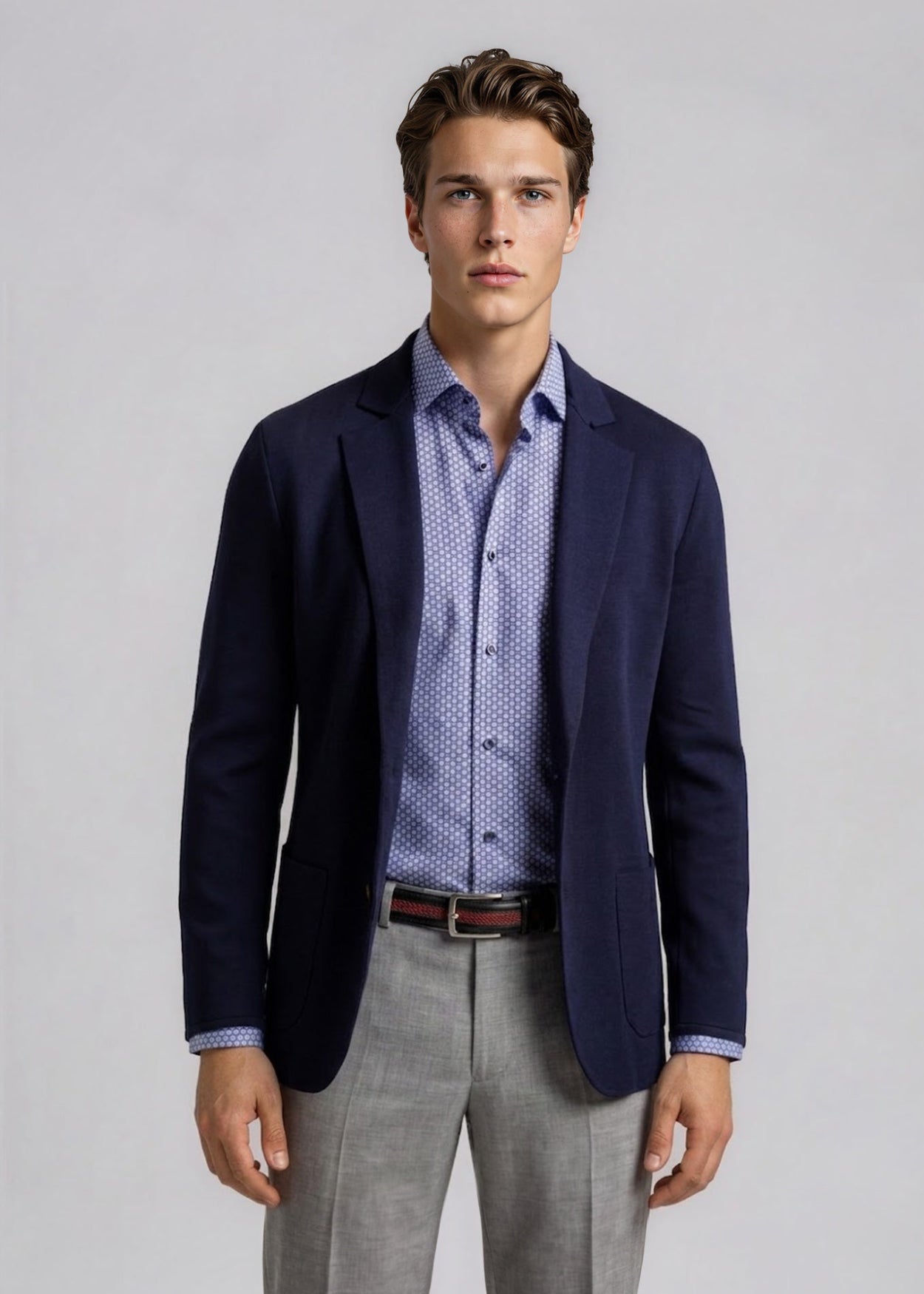 Man wearing a navy blazer, patterned shirt, and gray pants on a light gray background
