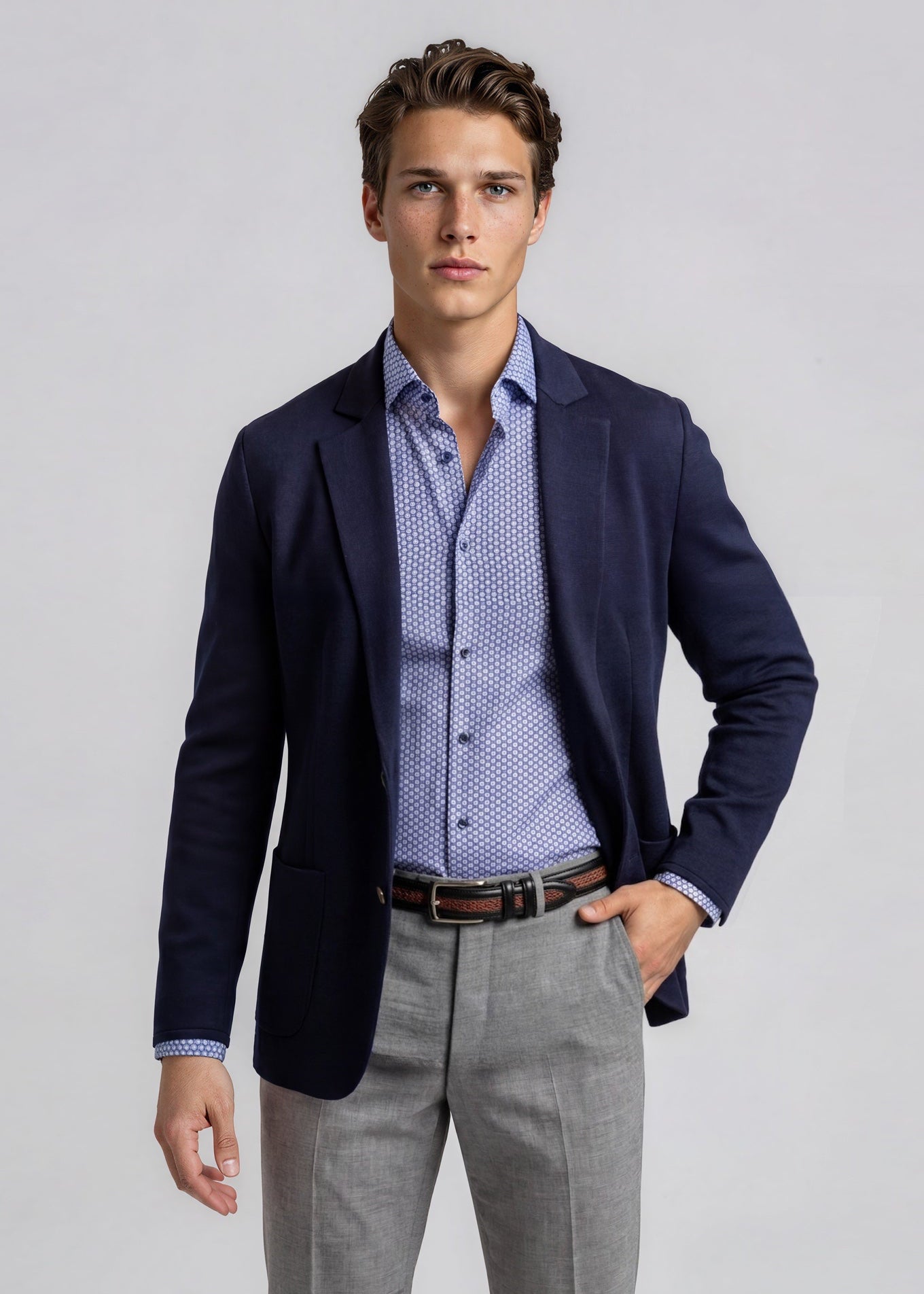 Man wearing a navy blazer, patterned shirt, and gray pants on a light gray background