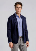 Man wearing a navy blazer, light blue patterned shirt, and gray pants on a plain background