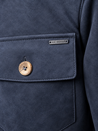 Close-up of a navy blue suede jacket pocket with a wooden button and a small metal brand plaque reading IKE BEHAR.