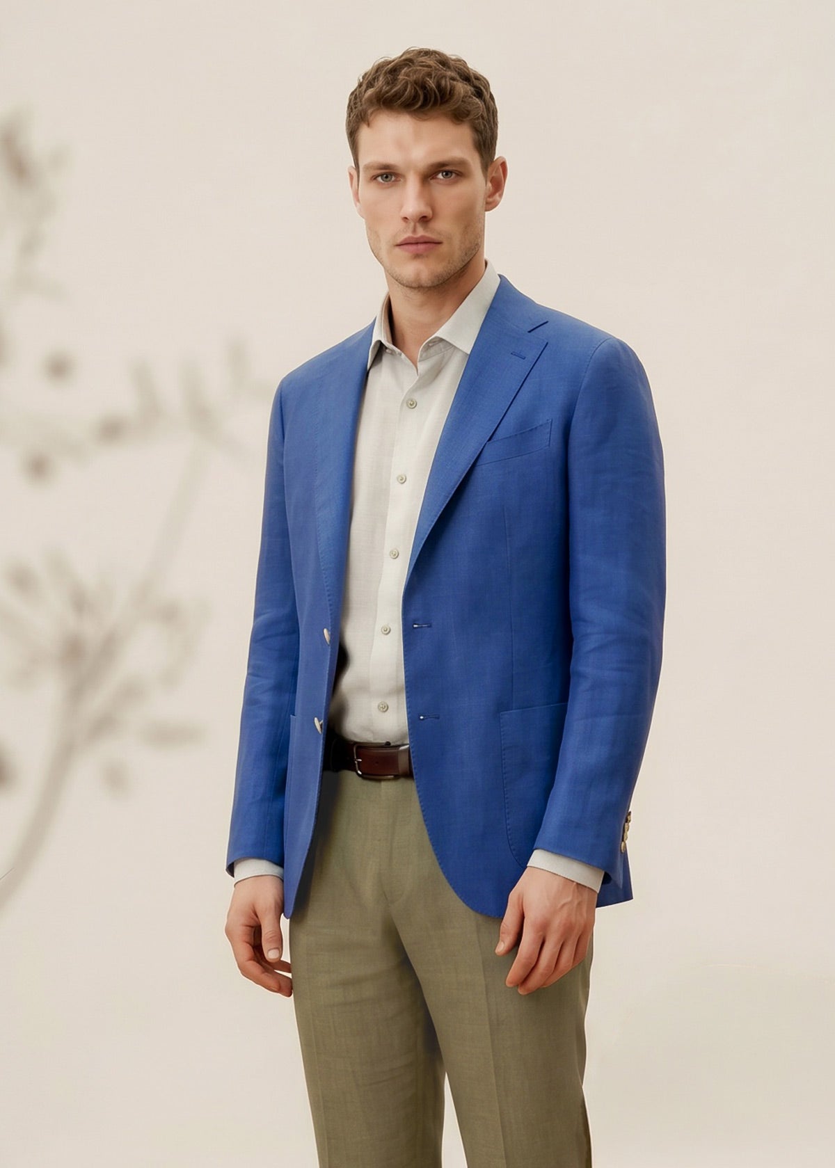 Man wearing a blue blazer, white shirt, and beige pants against a neutral background