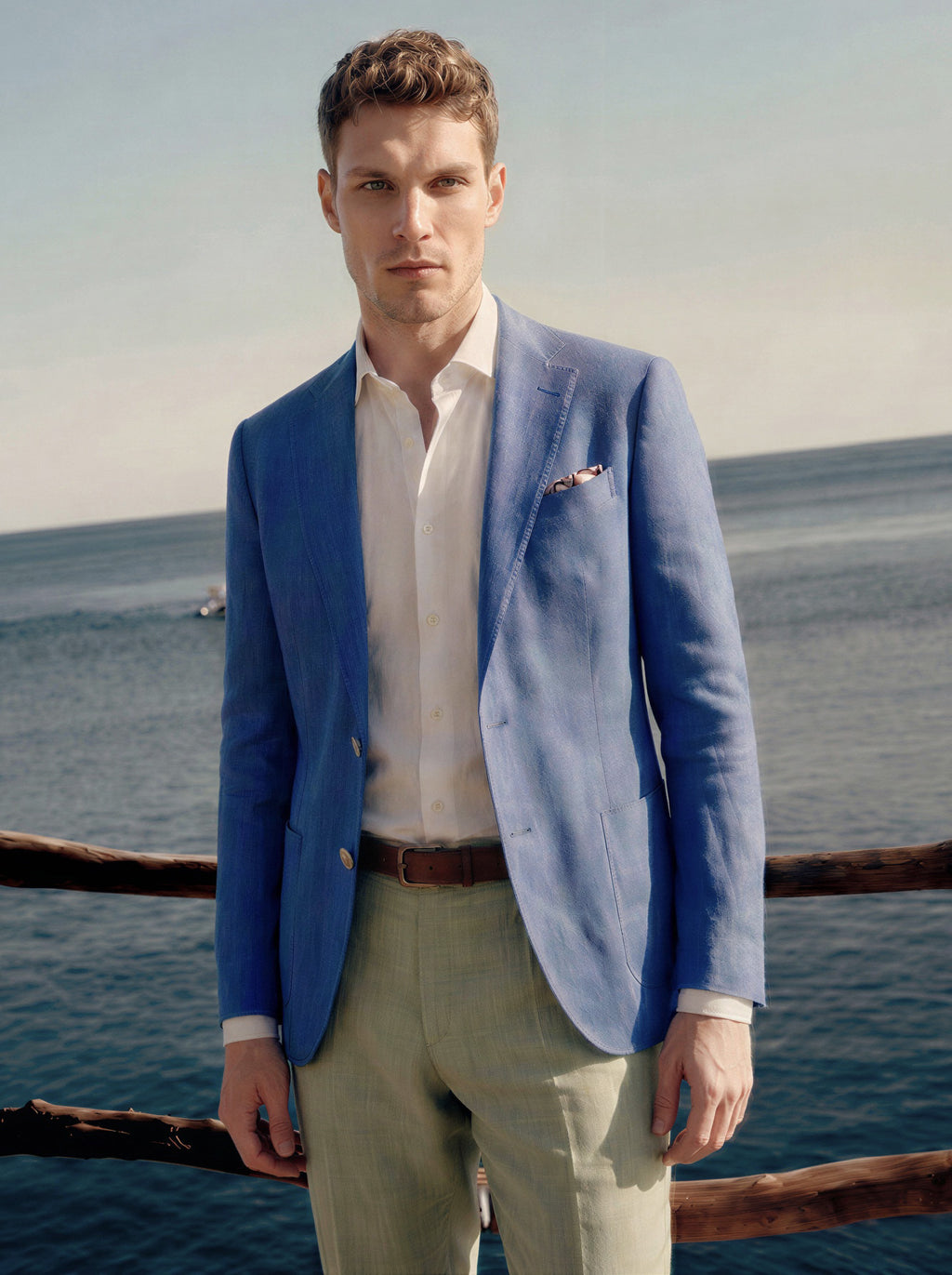 Man wearing a blue blazer and light green pants standing by a body of water.