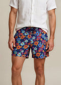 Man wearing a white shirt and colorful floral shorts on a beige background