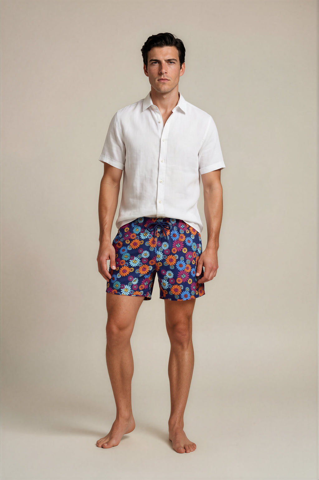 Man wearing a white shirt and colorful floral bathing suit shorts on a beige background