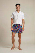 Man wearing a white shirt and colorful floral bathing suit shorts on a beige background