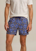 Man wearing a white polo shirt and blue patterned shorts on a beige background