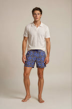 Man wearing a white polo shirt and blue patterned shorts on a beige background