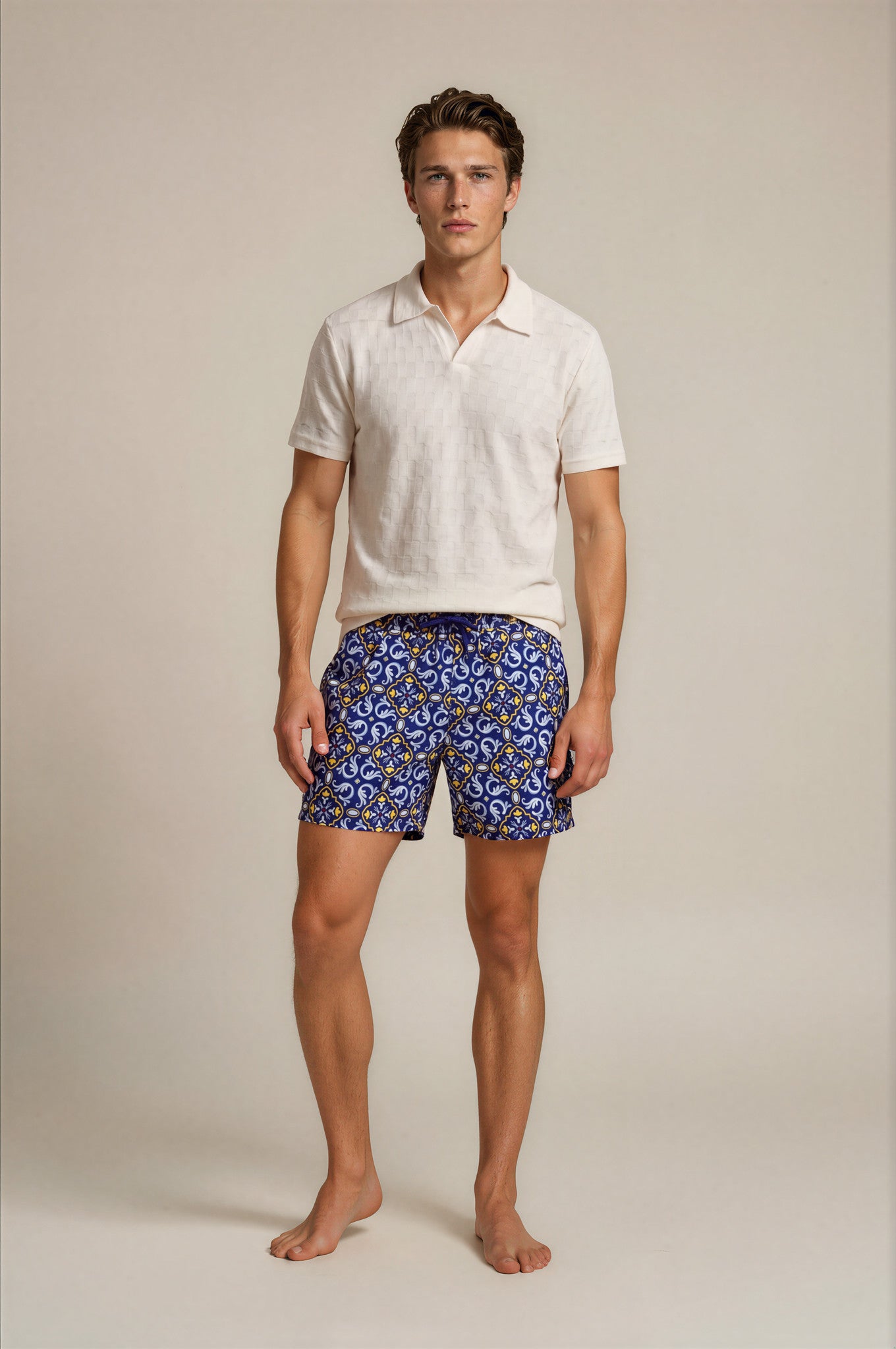 Man wearing a white polo shirt and blue patterned shorts on a beige background