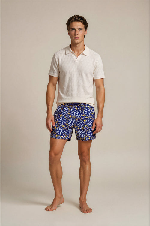 Man wearing a white polo shirt and blue patterned shorts on a beige background