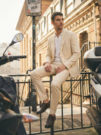 Man in a beige suit sitting on a railing with motorcycles in the foreground.