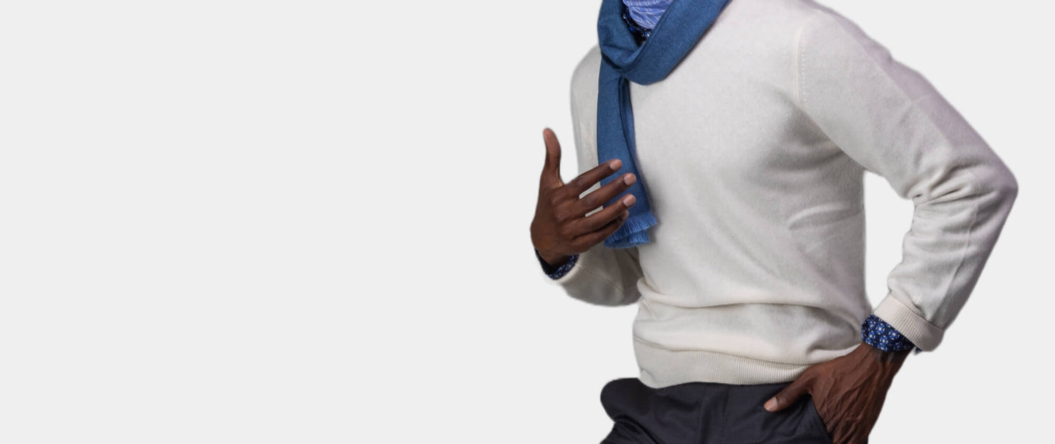 Torso of model wearing white Ike Behar sweater and blue scarf, hand in pocket