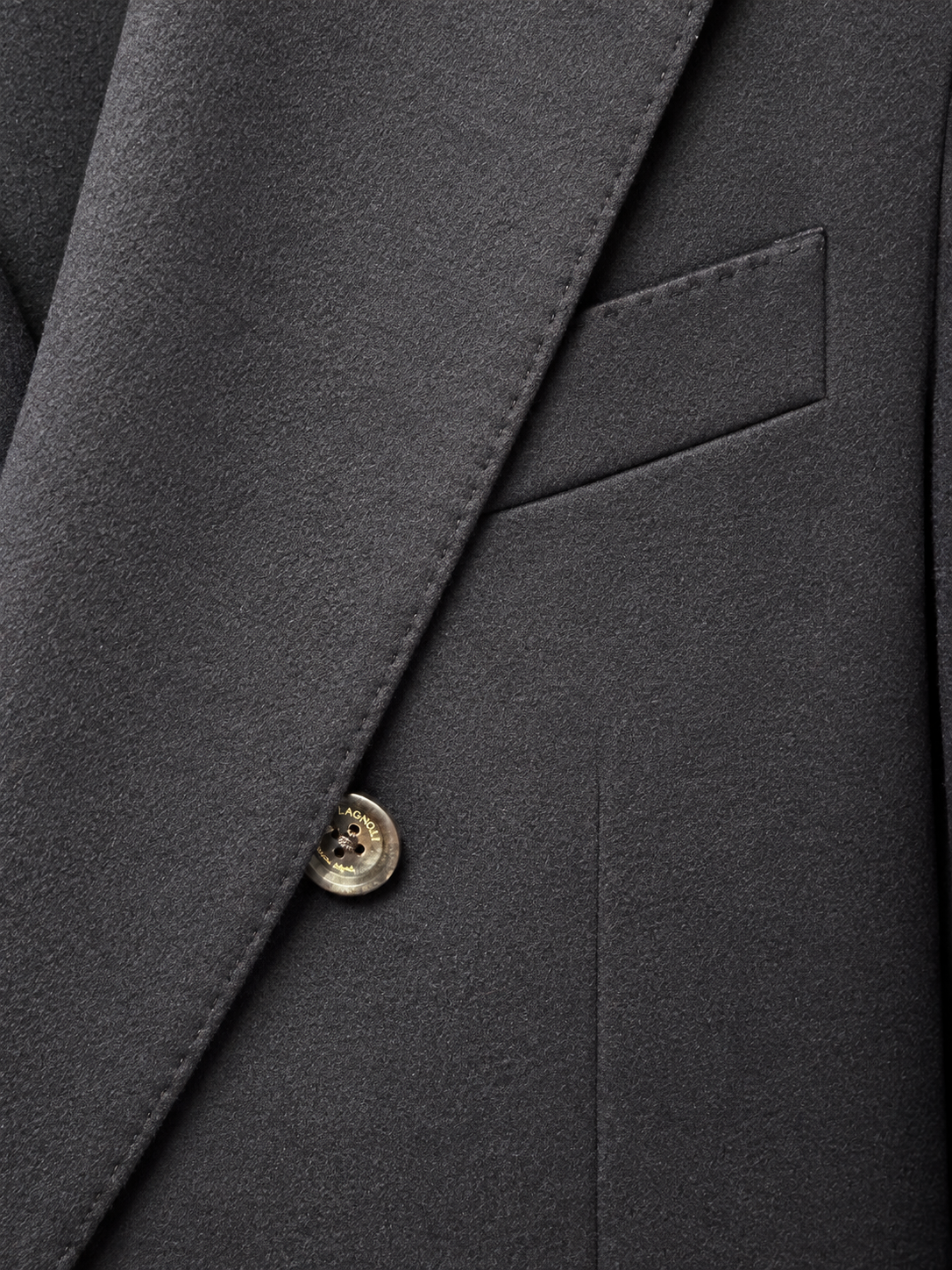 Close-up of a dark charcoal gray suit jacket showing the lapel, fine fabric texture, a welt pocket, and a single metallic button.