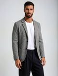 Man wearing a gray blazer over a white shirt and dark pants on a light gray background