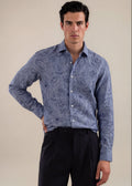 A man modeling a long-sleeve button-up shirt with a blue floral pattern, paired with black trousers, against a solid beige background.