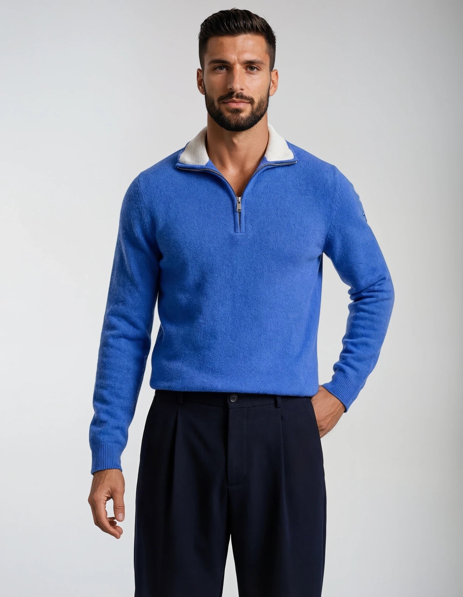 Man wearing a quarter zip blue sweater with a white collar against a gray background