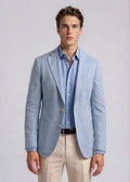 Man wearing a light blue blazer over a checkered shirt with beige pants on a plain background