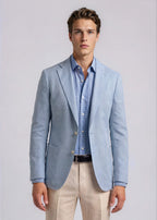 Man wearing a light blue blazer over a checkered shirt with beige pants on a plain background