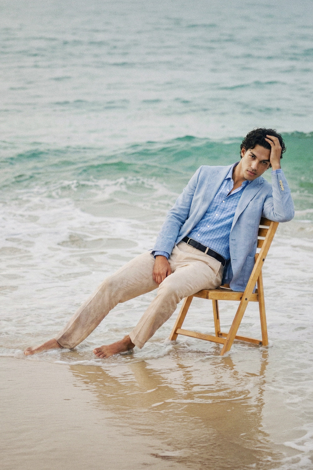 Man in sky blazer sitting on a wooden chair in the water at the beach