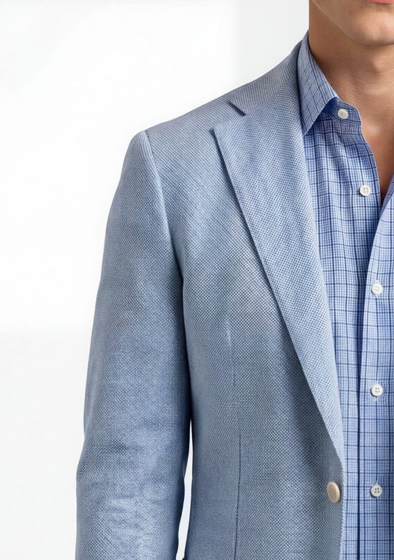 Man wearing a light blue blazer over a checkered shirt with beige pants on a white background