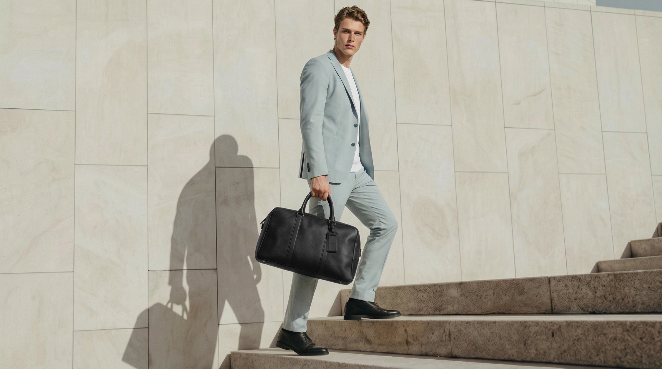 Man in light sky suit holding a black briefcase on stone steps.